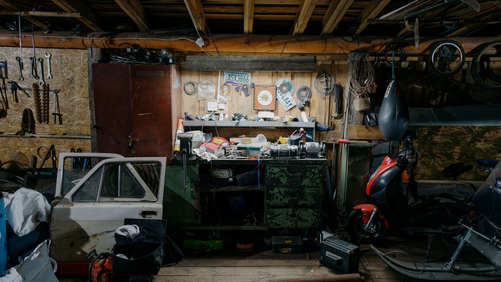 Eine vollgestellte Garage mit Werkzeug, Autotür, Motorroller und Kisten.